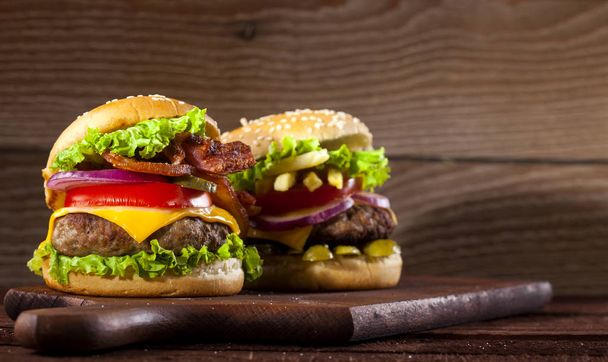 Sığır eti, domates, peynir, salatalık, soğan ve marul üzerine ahşap arka plan kopya alanı ile iki farklı lezzetli burger - Fotoğraf, Görsel