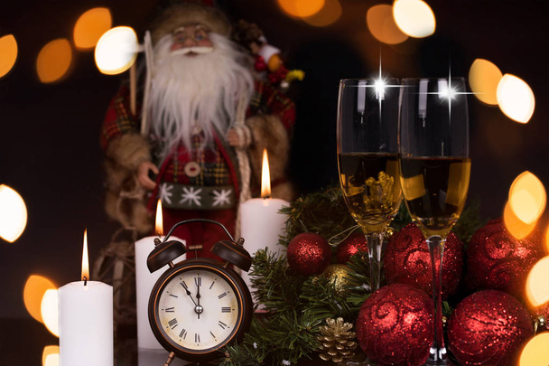 Two wine glasses with champagne, Santa Claus, clock, candles and christmas gifts on a black background with reflection. Copy space. Merry Christmas and Happy New Year, background - Photo, Image