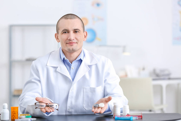 Male doctor holding contact lens case and glasses indoors - Фото, зображення