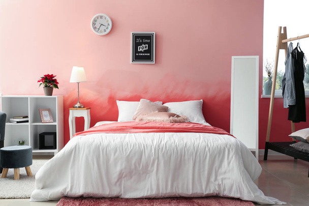 Interior de la habitación con cama cómoda cerca de la pared rosa
 - Foto, Imagen