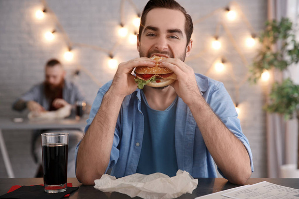 Man eating yummy burger in cafe - Foto, Imagem