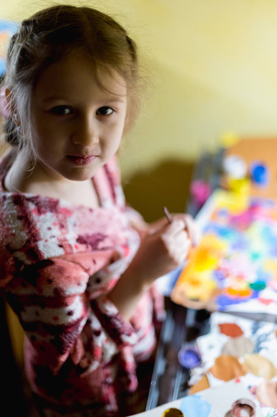 Cute little girl painting with paintbrush and colorful paints in home interior. - Photo, Image
