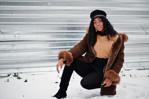 African american woman in sheepskin coat and cap posed at winter day against snowy background. - Foto, Imagen