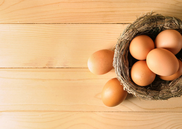 Гнездо с сырыми коричневыми куриными яйцами на деревянном столе
 - Фото, изображение