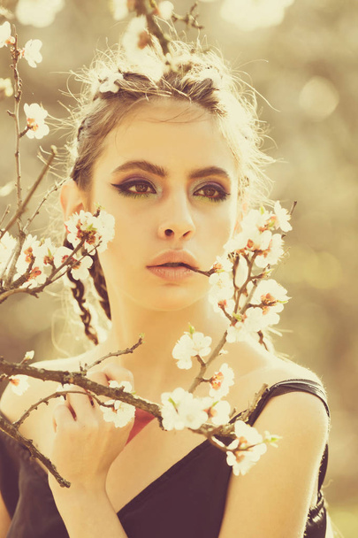 pretty girl with fashionable makeup among spring blooming cherry flowers - Foto, afbeelding