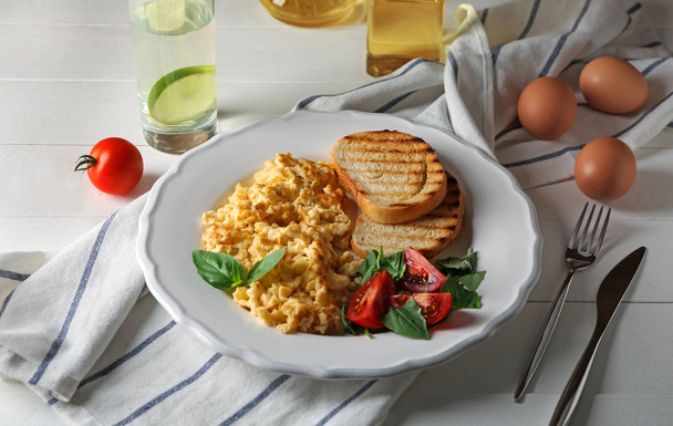 Assiette avec omelette savoureuse et pain grillé sur table en bois blanc
 - Photo, image