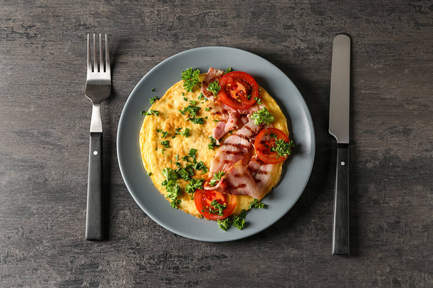 Teller mit leckerem Omelett und Speck auf grauem Tisch - Foto, Bild