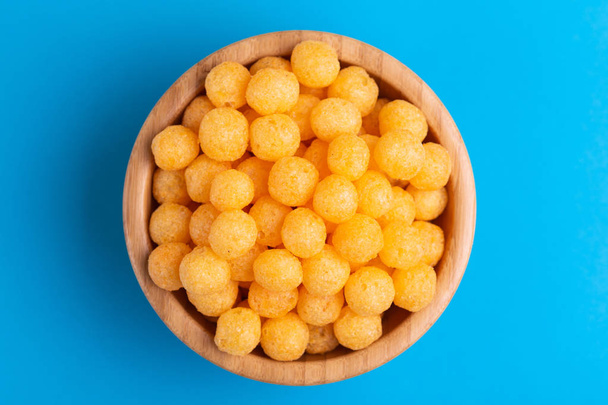 Cheese puff balls in wooden bowl on bright colorful background. Cinema snacks. Copy space - Fotó, kép