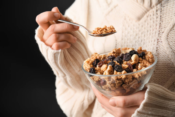 Woman eating tasty granola with dried fruits on dark background - Foto, Imagem