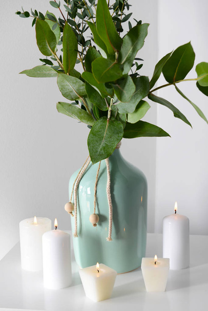 Queimando velas e vaso com galhos de eucalipto na mesa branca
 - Foto, Imagem