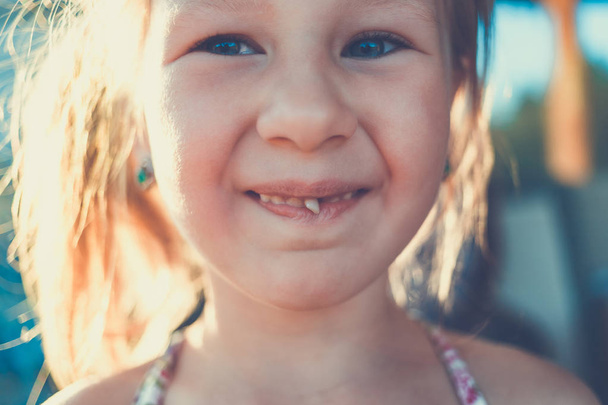 Porträt eines kleinen Mädchens mit ausgestrecktem Milchzahn. - Foto, Bild