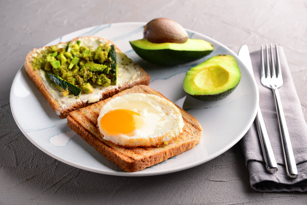 Тарілка з підсмаженим хлібом, авокадо та смаженим яйцем на сірому столі
 - Фото, зображення