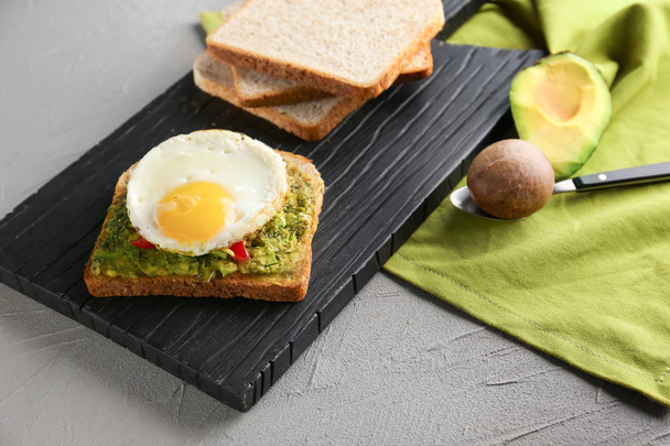Вкусный жареный хлеб с авокадо и жареным яйцом на деревянной доске
 - Фото, изображение