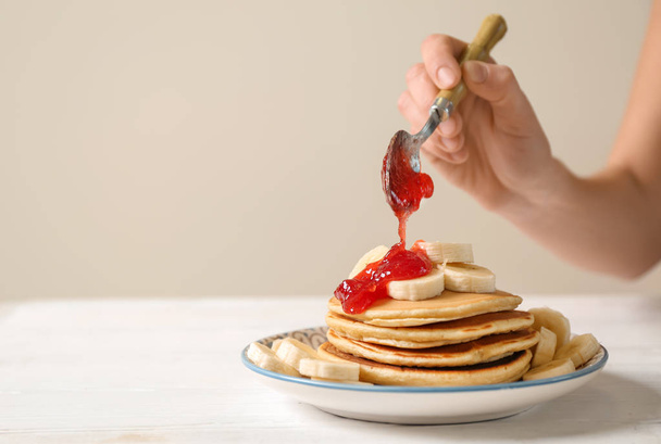 Woman adding jam to tasty pancakes with banana slices on plate - Foto, Imagem