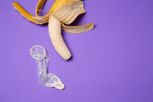 Banaan en condoom met witte vloeistof op kleur achtergrond. Erotische concept - Foto, afbeelding