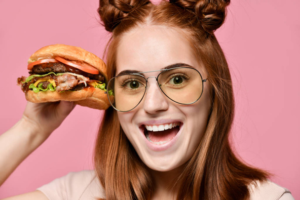 Close up portrait of a hungry young woman eating burger isolated over pink background - Фото, зображення