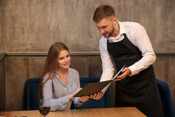 Młody kelner, pokazując kobieta menu w restauracji - Zdjęcie, obraz