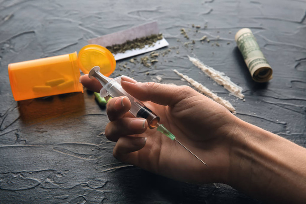 Female junkie with syringe and drugs at dark table. Concept of addiction - Valokuva, kuva