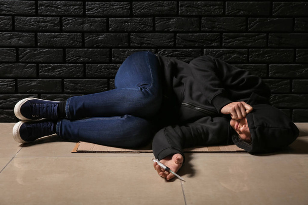 Női drogos fecskendővel sötét téglafal közelében fekve. A függőség fogalma - Fotó, kép