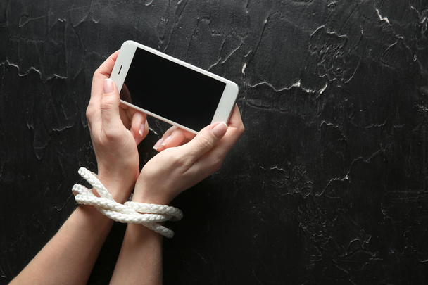 Женщина со связанными руками и мобильным телефоном на темном фоне. Концепция зависимости
 - Фото, изображение