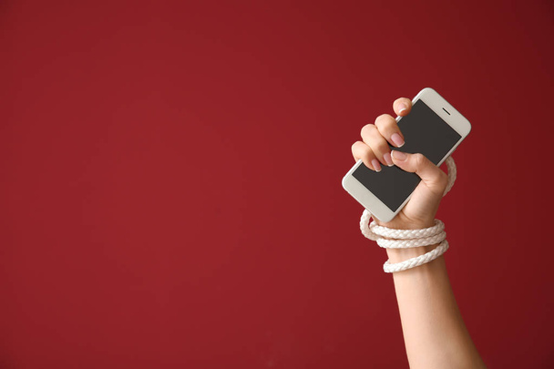 Γυναίκα με δεμένα χέρι και το κινητό τηλέφωνο στο χρώμα φόντου. Έννοια της εξάρτησης - Φωτογραφία, εικόνα
