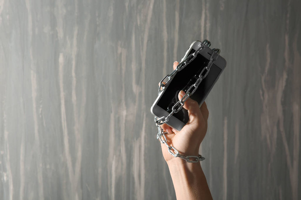 Donna con mano incatenata e cellulare su sfondo grigio. Concetto di dipendenza
 - Foto, immagini