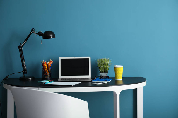 Стильное рабочее место с современным ноутбуком рядом с цветной стеной - Фото, изображение