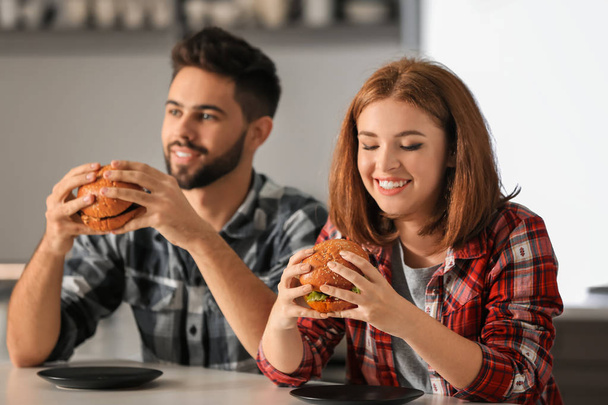 Young couple eating tasty burgers at home - Fotoğraf, Görsel