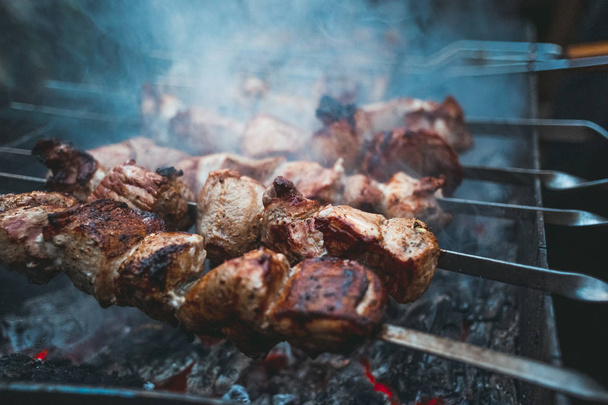 Grilled kebab cooking on metal skewers (grill). Roasted meat cooked at barbecue with smoke. Close up BBQ fresh pork meat chop slices. Traditional eastern dish, shish kebab. Grill on charcoal and flame, picnic, street food. Toned, style, classic photo - Foto, immagini