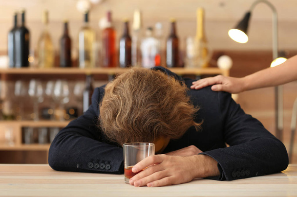 Woman trying to wake up drunk man with glass of whiskey in bar. Alcoholism concept - Photo, Image