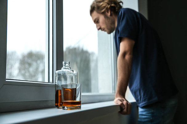 落ち込んだ若者の平らな窓ガラスにウイスキーのボトルとグラス。アルコール依存症の概念 - 写真・画像