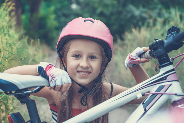 Little cute girl in a pink helmet near a bicycle in summer - Photo, Image