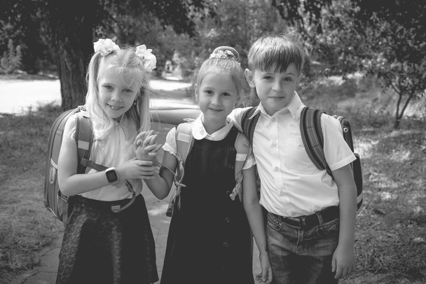 Three elementary school students with backpacks on the street. Monochrome photo. - Photo, Image