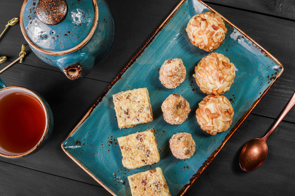 hausgemachte cremige Fudge Bonbons mit Kokos, Rosinen, Nüssen, Sesam, Erdnüssen, serviert auf dem Vintage-Teller mit Teekanne. Ansicht von oben - Foto, Bild