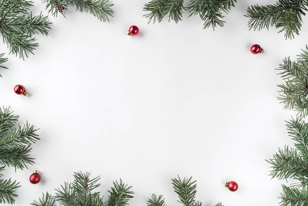 Kreativer Rahmen aus Tannenzweigen auf weißem Hintergrund mit roter Dekoration, Tannenzapfen. Weihnachts- und Neujahrsthema. flache Lage, Draufsicht - Foto, Bild