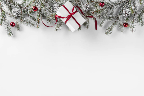 Рождественские подарочные коробки на белом фоне с еловыми ветвями, сосновыми шишками, красной лентой. Новогодняя тема. Плоский, вид сверху
 - Фото, изображение