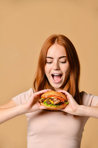 Close up portrait of a hungry young woman eating burger isolated over nude background - Foto, imagen