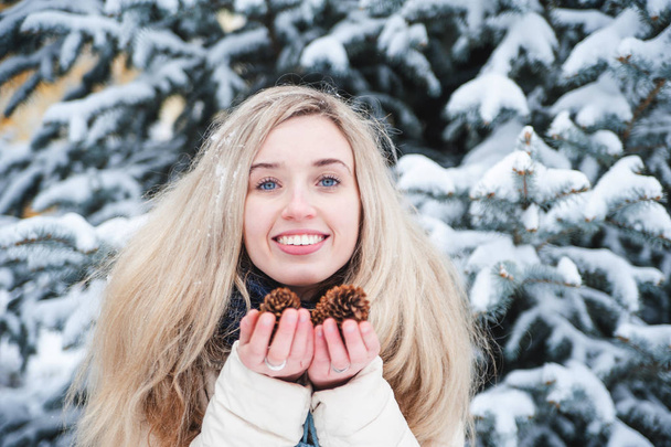 Mooie lachende vrouw houdt een pinecones in handen. Besneeuwde weer buiten. Levensstijl. Wintervakantie. - Foto, afbeelding