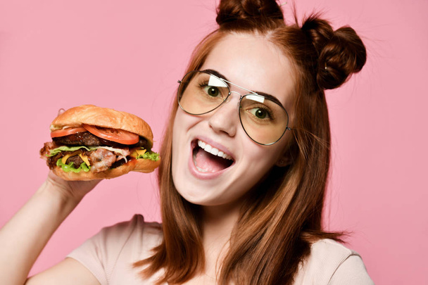 Horizontal studio shot of pretty young woman holding a burger and a glass of soda. - Foto, imagen