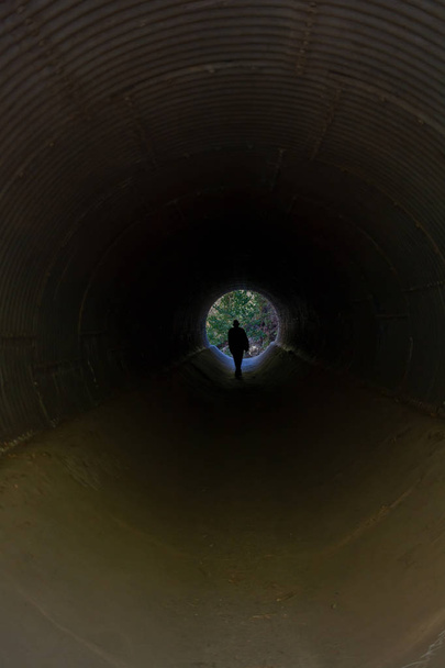 Silueta humana no identificable cruzando un túnel oscuro al final del cual hay concepto de muerte por luz o renacimiento
 - Foto, imagen