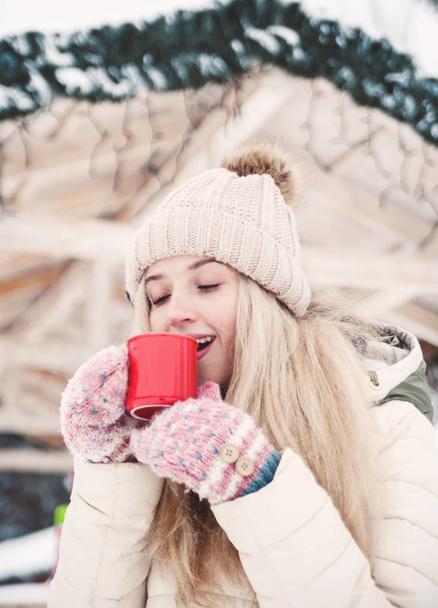 Sonriente hermosa joven bebe un cacao caliente al aire libre. Clima nevado. Vacaciones de invierno
. - Foto, imagen