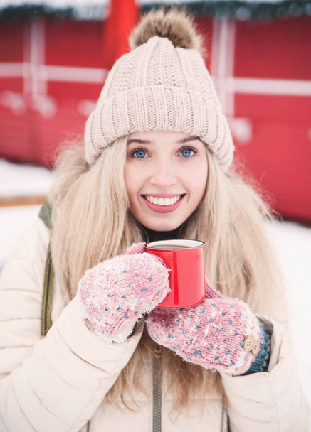 Lächelnd trinkt die schöne junge Frau einen heißen Kakao im Freien. Schneewetter. Winterurlaub. - Foto, Bild