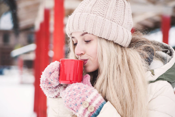 Smiling beautiful young woman drinks a hot cocoa outdoor. Snowy weather. Winter holidays. - Photo, Image
