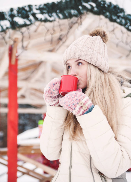 Sonriente hermosa joven bebe un cacao caliente al aire libre. Clima nevado. Vacaciones de invierno
. - Foto, Imagen