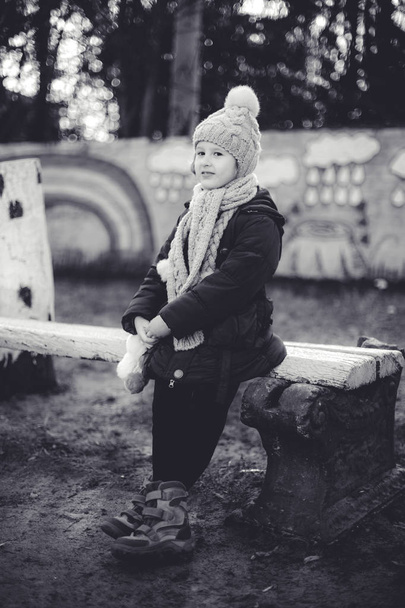 Μικρό χαριτωμένο κορίτσι που κάθεται στον πάγκο το χειμώνα. Μονόχρωμη φωτογραφία - Φωτογραφία, εικόνα