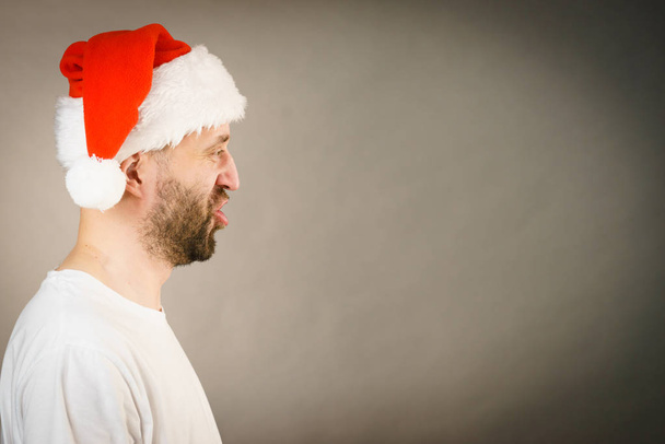 Homem barbudo usando chapéu de Papai Noel, vista lateral em cinza com espaço de cópia. Hora de Natal
. - Foto, Imagem