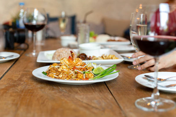 Słynny Pad tajski makaron z krewetkami i kieliszek czerwonego wina na drewnianym stole - Zdjęcie, obraz