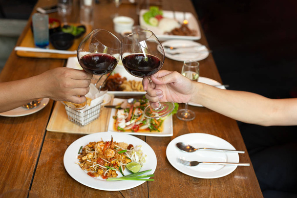 Freunde feiern Mittagessen mit Händen, die ein Glas Rotwein mit Essen anstoßen - Foto, Bild