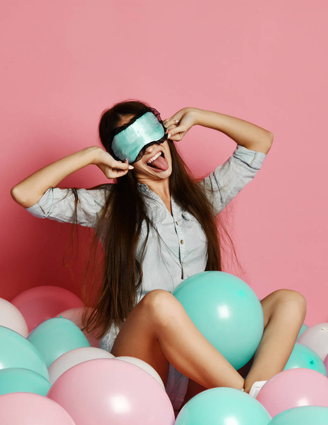Cute caucasian sexy woman in sleep mask having fun with colorful balloon over pink background - 写真・画像