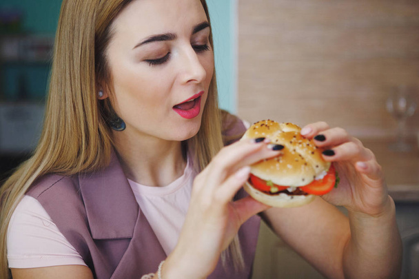 hübsche junge Frau bereit, einen riesigen Hamburger zu essen. öffnete sie den Mund in Erwartung des gastronomischen Genusses. das Konzept der gesunden Ernährung, der Kampf gegen Übergewicht. - Foto, Bild